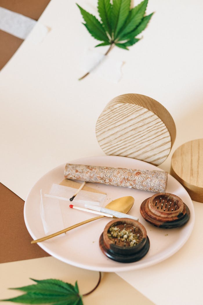 Cannabis-themed flat lay with a joint, grinder, and leaves on a pastel background.